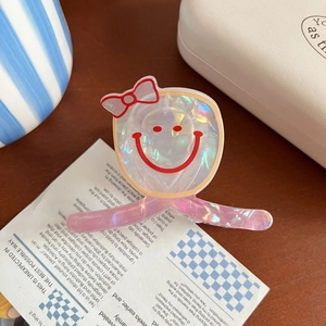 Détail d'une pince à cheveux en acrylique laser avec motif smiley et nœud rouge