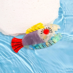 Colorful fish-shaped acetate hair claw clip displayed on a white stone background