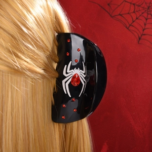 Détail d'une pince à cheveux araignée gothique avec strass rouges sur cheveux blonds