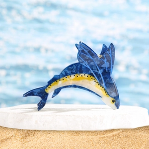 Dettaglio della molletta per capelli in acetato blu a forma di pesce sulla spiaggia