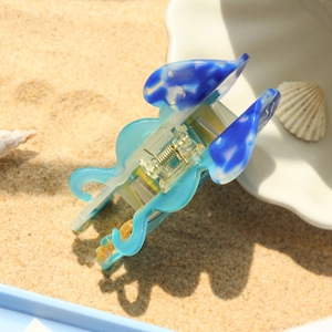 Dettaglio della molletta per capelli a medusa blu mare con trama in marmo sulla spiaggia