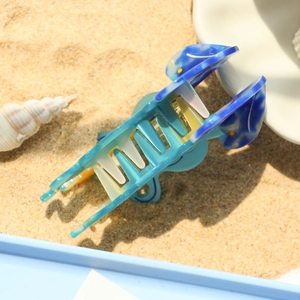 Dettaglio della grande molletta per capelli blu effetto marmo su una spiaggia di sabbia