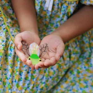 Barrette à cheveux cigale avec ailes irisées et acétate vert sur robe à fleurs
