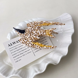Detail of a bird-shaped hair claw clip with acetate tortoiseshell texture on a white tray