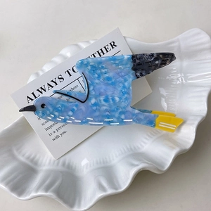Detail of the bird-shaped blue and yellow cellulose acetate hair claw clip in a shell tray
