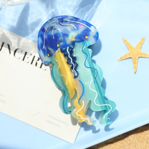 Dettaglio del fermaglio a forma di medusa in acetato marmorizzato blu su sfondo spiaggia