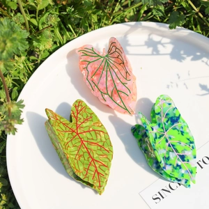 Three leaf-shaped cellulose acetate hair claws with marble textures on a white tray