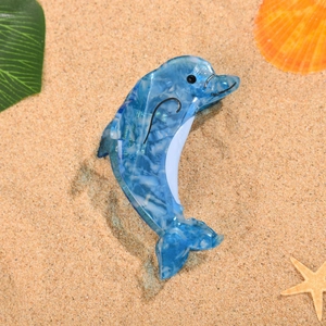 Détail d'une pince à cheveux dauphin en acétate marbré bleu sur sable fin