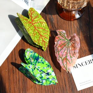 Detailed view of three leaf-shaped acetate hair claws with marble textures on a wooden surface