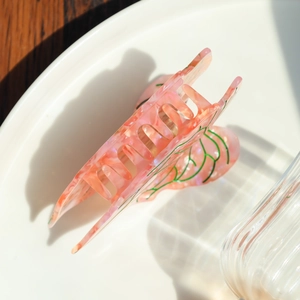Detailed close-up of pink shell acetate hair claw clip with green leaf vein patterns