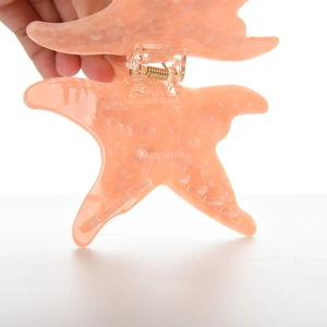 Gros plan d'une pince à cheveux étoile de mer rose marbré avec ressort doré et dents