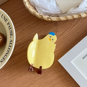 Détail d'une pince à cheveux canard jaune en acétate posée sur une table en bois chaud