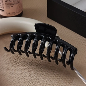 Close-up of large glossy black shark hair claw clip with smooth teeth on a wooden surface