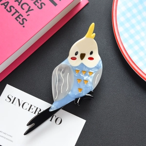 Dettaglio della molletta per capelli a forma di pappagallo blu e bianco in acetato marmorizzato