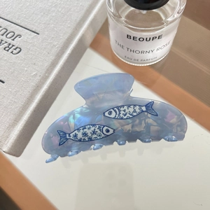 Detailed view of a light blue pearlescent shark hair clip with fish patterns and texture