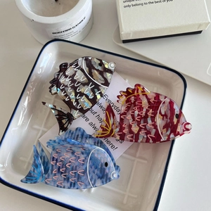 Three acetate fish hair claws in ocean colors arranged in a ceramic tray for styling
