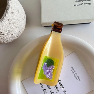 Detail view of champagne bottle hair claw clip with grape motif on ceramic plate