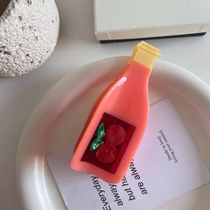 Detail view of a pink bottle-shaped peach hair claw clip with cherry motif on white tray