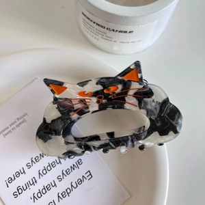Détail d'une pince à cheveux chat en acétate avec motif marbré noir et blanc et accents orange