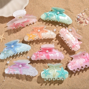 Flat lay of colorful starfish hair claws with pearls on a sandy beach background