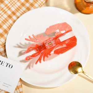 Pince à cheveux créative en forme de homard orange posée sur une assiette