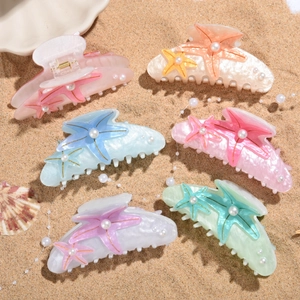 Set of colorful starfish hair claws with pearls on a sandy beach background