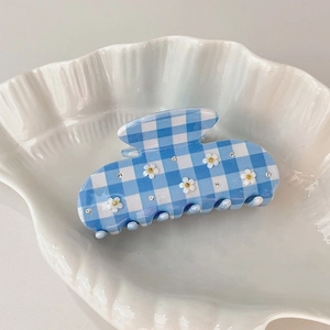 Macro view of blue checkered acetate hair claw with white daisy and diamond accents