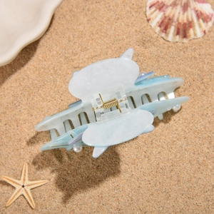 Detailed close-up of a blue starfish hair claw with pearls on a beach setting