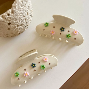 Floral acetate hair claw clips set with daisy flowers and rhinestones on desk