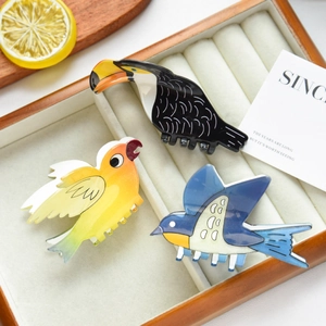 Three colorful bird-shaped hair claws including toucan and swallow designs in a gift box