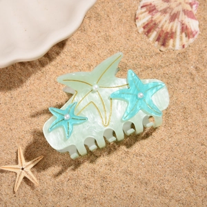 Detail of sea star hair claw clip with pearls on a beach background with sand and shells