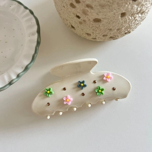 Detail of cream acetate claw clip with 3D floral accents and brown rhinestones