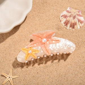 Detail view of starfish hair claw clip with pearls on sand beach background