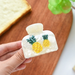 Detailed view of cream acetate hair claw clip featuring small pineapple accents