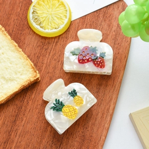 Detail view of acetate hair claws featuring strawberry and pineapple fruit patterns
