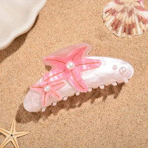 Detailed view of starfish claw clip with faux pearls on sandy beach background
