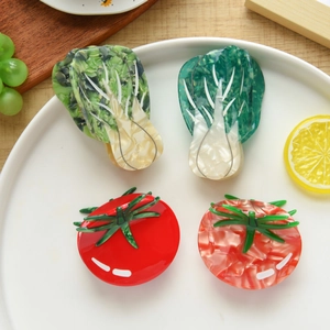 Detail of four acetate hair claws shaped like cabbage and tomato on a white plate