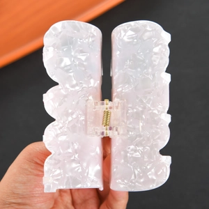 Macro view of creamy white marble texture hair claw clip with golden metal spring