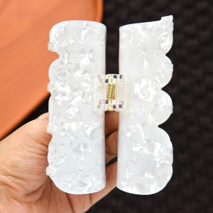 Close-up of a white marble acetate hair claw clip with wavy edges and gold metal spring