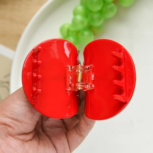 Macro detail of red apple-shaped hair claw clip with golden spring and inner teeth