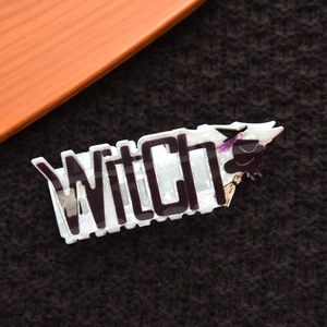Detail view of white marble acrylic hair claw clip with black Witch text and cartoon design