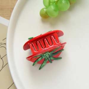Detailed macro view of a red tomato-shaped acetate hair claw clip on a white plate