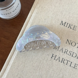 Detailaufnahme der perlmuttfarbenen Acetat-Haarklammer mit Goldschrift auf einem Buch