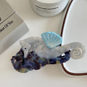 Detail view of seahorse-shaped hair claw clip with blue and white marble textures
