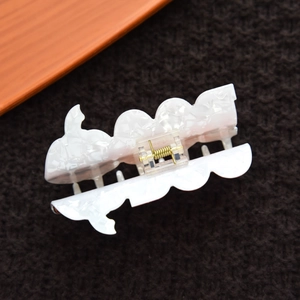 Close-up of white marble acetate hair claw clip with golden metal spring and wave design