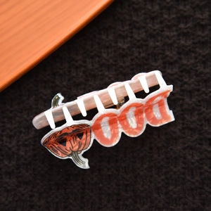 Detail showing white acetate hair claw with orange pumpkin and BOO text for Halloween