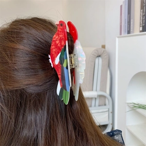 Détail d'une pince à cheveux perroquet rouge en acétate sur de longs cheveux bruns
