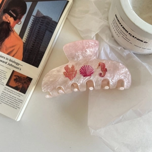 Dettaglio della pinza per capelli in marmo rosa con motivi di coralli e conchiglie