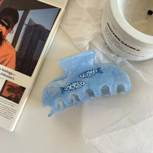 Dettaglio della pinza per capelli in marmo blu con motivi a pesce su sfondo raffinato