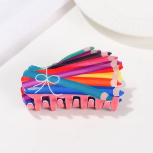 Detail of colorful pencil pattern acetate claw clip with white bow on white fabric